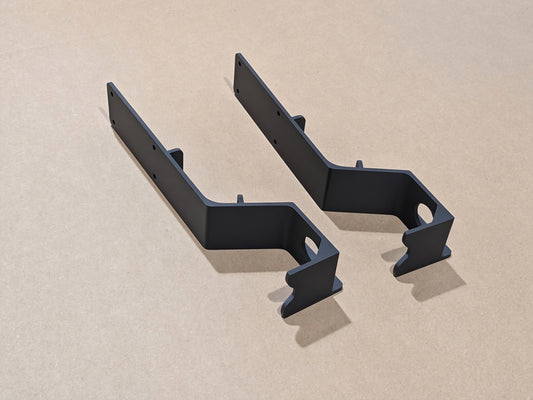 Two matte black elddis tap brackets with pre-drilled screw holes, displayed on a light beige textured background.